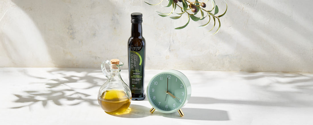 Dark bottle of extra virgin olive oil pressed within hours of harvest, with golden oil and olive branch on marble