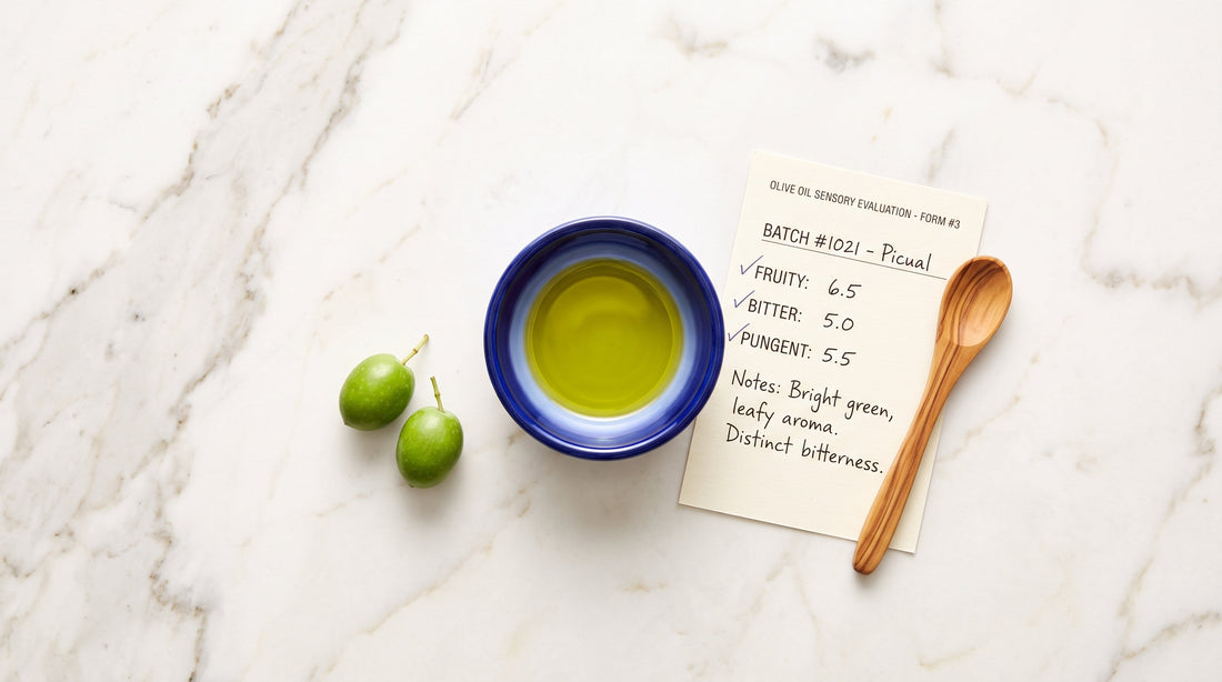 Blue olive oil tasting cup and pungency scoring sheet on white marble. The one-cough test for measuring oleocanthal in high polyphenol olive oil.